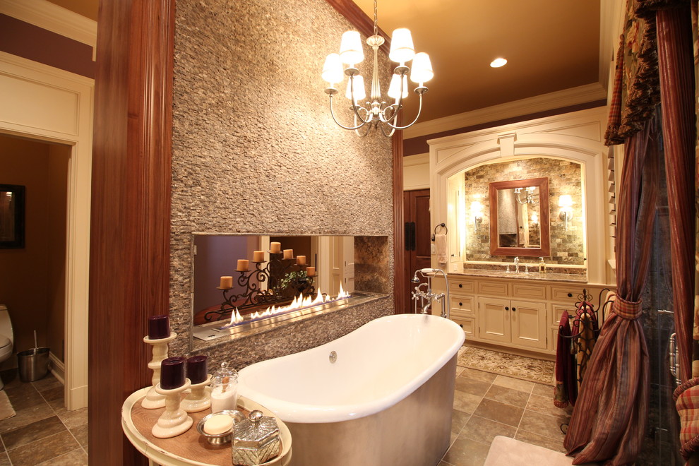 Photo of an expansive traditional master bathroom in Cleveland with an undermount sink, recessed-panel cabinets, white cabinets, granite benchtops, a freestanding tub, a two-piece toilet, brown tile, stone tile, brown walls and porcelain floors.