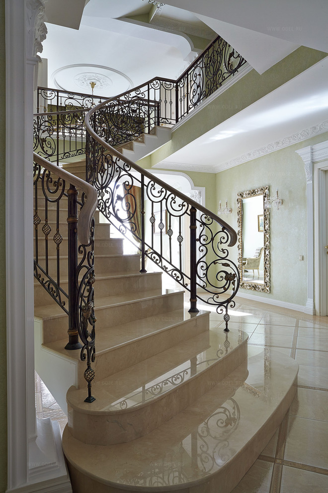 Large traditional travertine curved staircase in Moscow with travertine risers and wood railing.