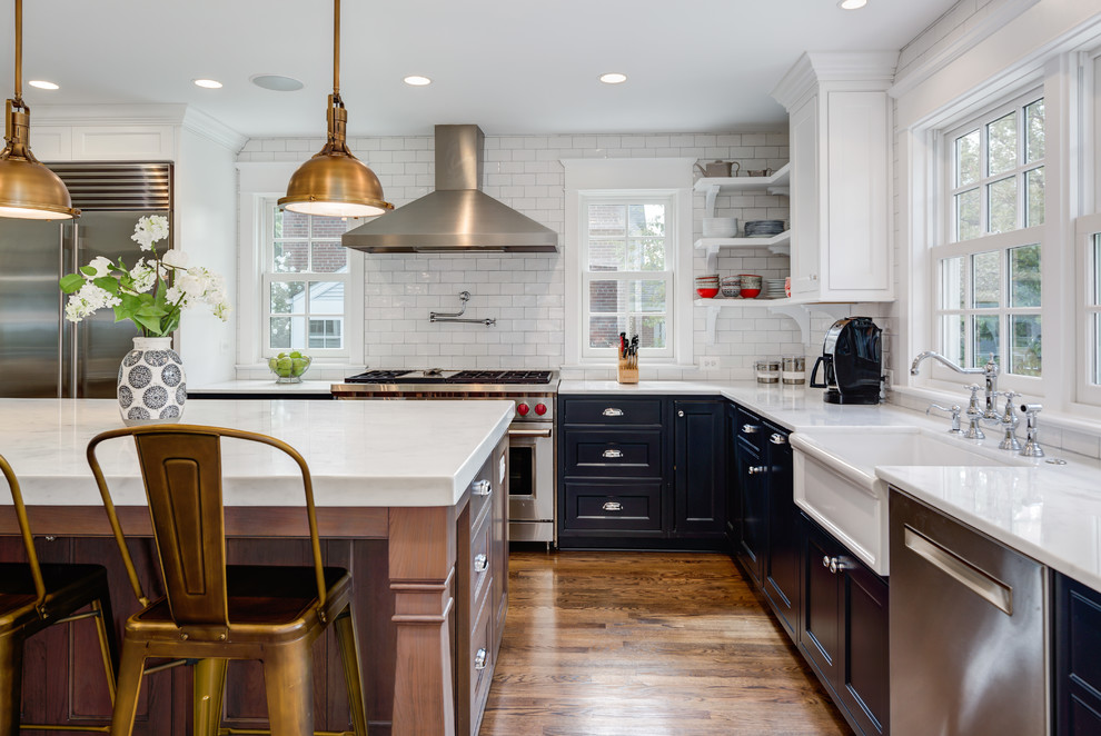 Photo of a large transitional l-shaped open plan kitchen in DC Metro with a farmhouse sink, shaker cabinets, white cabinets, quartz benchtops, white splashback, subway tile splashback, stainless steel appliances, medium hardwood floors, with island, brown floor and white benchtop.