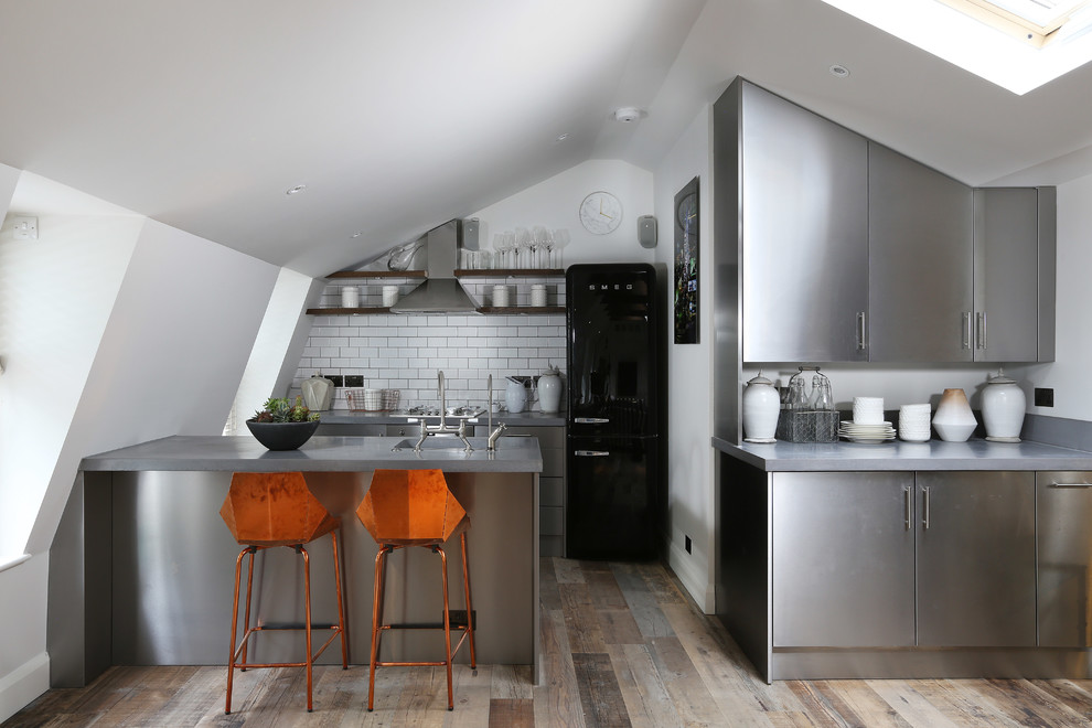 This is an example of a contemporary kitchen in London with flat-panel cabinets, stainless steel cabinets, stainless steel benchtops, white splashback, subway tile splashback, stainless steel appliances, a peninsula and dark hardwood floors.