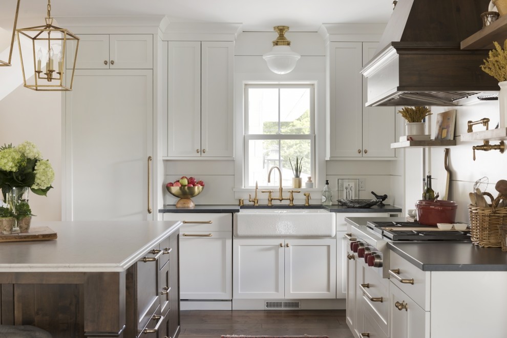 Country l-shaped kitchen in Miami with a farmhouse sink, shaker cabinets, white cabinets, white splashback, dark hardwood floors, with island, brown floor and black benchtop.