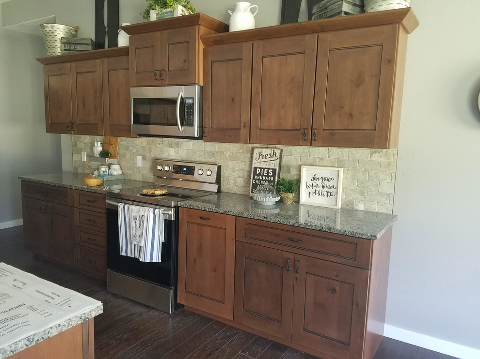 Mid-sized mountain style single-wall dark wood floor and brown floor open concept kitchen photo with an undermount sink, shaker cabinets, dark wood cabinets, granite countertops, beige backsplash, stone tile backsplash, stainless steel appliances and an island