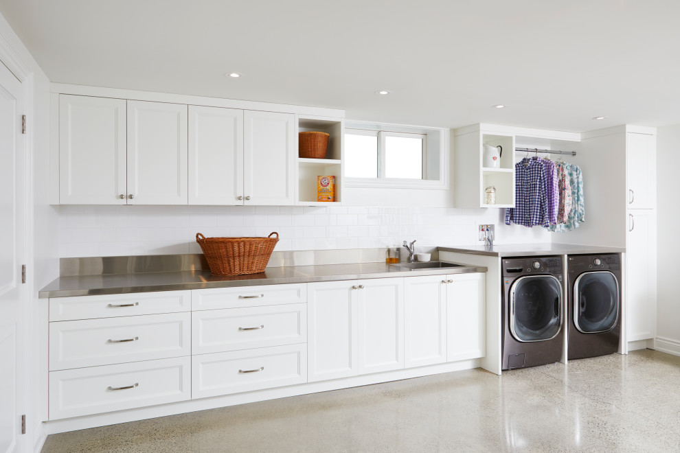 Design ideas for an expansive traditional single-wall utility room in Toronto with an integrated sink, recessed-panel cabinets, white cabinets, stainless steel benchtops, white walls, concrete floors, a side-by-side washer and dryer and grey floor.