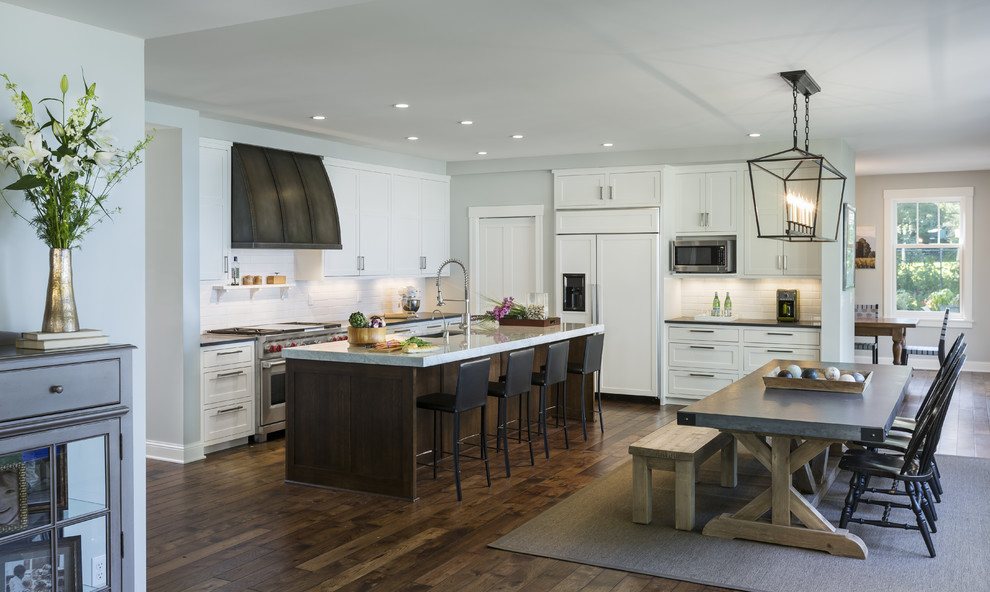 This is an example of a transitional l-shaped eat-in kitchen in Minneapolis with shaker cabinets, white cabinets, white splashback, subway tile splashback, stainless steel appliances, dark hardwood floors and with island.