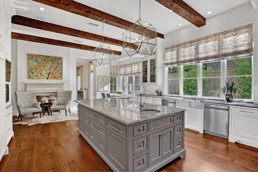 Mediterranean u-shaped open plan kitchen in Dallas with a farmhouse sink, recessed-panel cabinets, grey cabinets, white splashback, stainless steel appliances, medium hardwood floors, with island and brown floor.