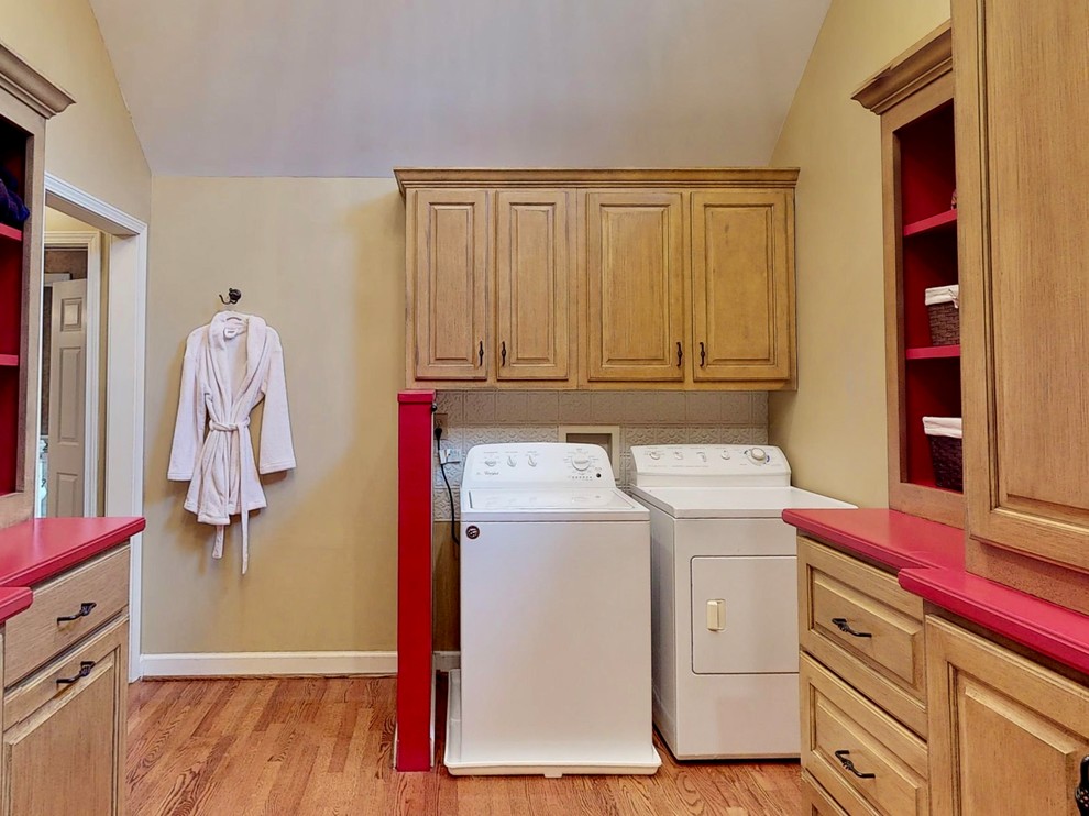 Design ideas for a mid-sized u-shaped dedicated laundry room in Other with raised-panel cabinets, light wood cabinets, solid surface benchtops, beige walls, light hardwood floors, a side-by-side washer and dryer and red benchtop.