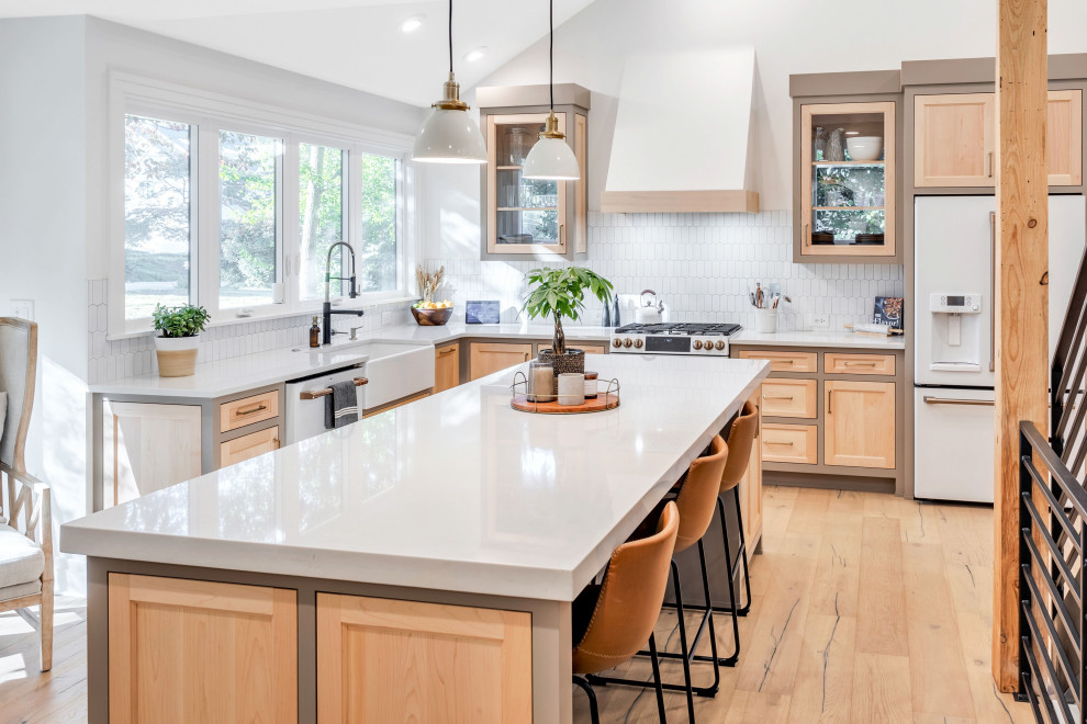 Mid-sized country eat-in kitchen in Other with a farmhouse sink, recessed-panel cabinets, light wood cabinets, solid surface benchtops, white splashback, subway tile splashback, white appliances, light hardwood floors, with island, brown floor, white benchtop and vaulted.