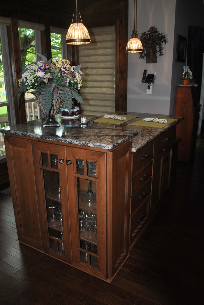 Example of a brown floor kitchen design with brown cabinets, an island, gray countertops, beige backsplash and stainless steel appliances