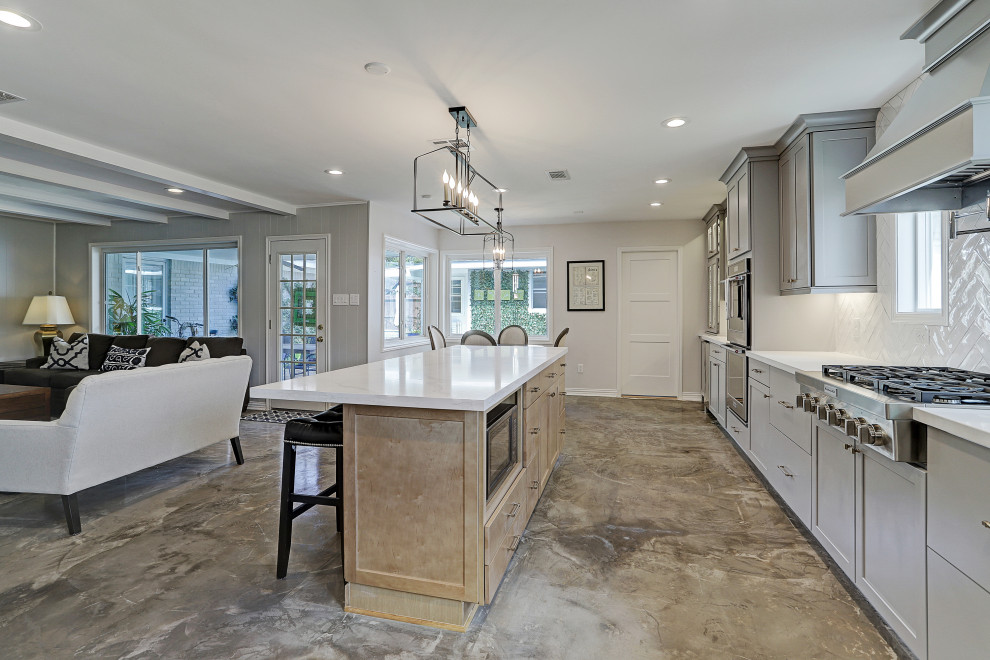Inspiration for a mid-sized traditional galley open plan kitchen in Houston with a farmhouse sink, recessed-panel cabinets, grey cabinets, granite benchtops, white splashback, subway tile splashback, stainless steel appliances, cement tiles, with island, grey floor and white benchtop.