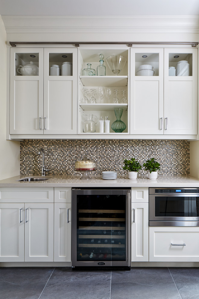This is an example of a small transitional single-wall wet bar in Toronto with an undermount sink, shaker cabinets, white cabinets, quartz benchtops, mosaic tile splashback, porcelain floors, grey floor, beige benchtop and multi-coloured splashback.