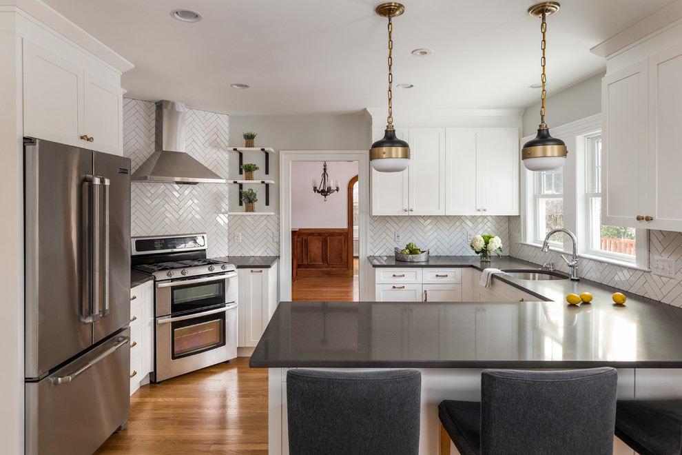 Inspiration for a mid-sized transitional u-shaped brown floor and medium tone wood floor enclosed kitchen remodel in Boston with an undermount sink, shaker cabinets, white cabinets, quartz countertops, ceramic backsplash, stainless steel appliances, a peninsula, gray countertops and white backsplash