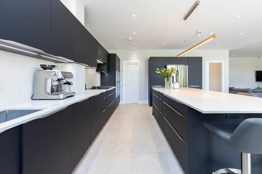 This is an example of a large modern galley open plan kitchen in Hertfordshire with a single-bowl sink, flat-panel cabinets, black cabinets, concrete benchtops, white splashback, black appliances, ceramic floors, with island, grey floor and white benchtop.