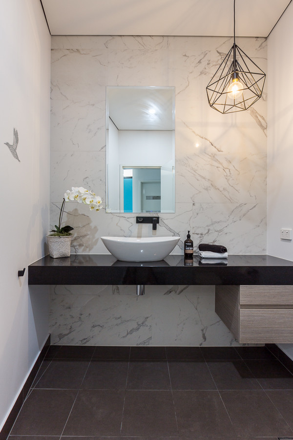 This is an example of a mid-sized contemporary powder room in Perth with flat-panel cabinets, light wood cabinets, white tile, white walls, a vessel sink, engineered quartz benchtops and black floor.