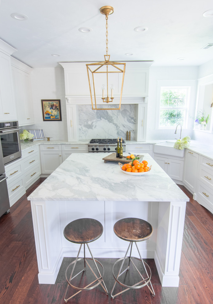 Inspiration for a transitional u-shaped dark wood floor and brown floor kitchen remodel with a farmhouse sink, shaker cabinets, white cabinets, marble countertops, marble backsplash, stainless steel appliances and an island