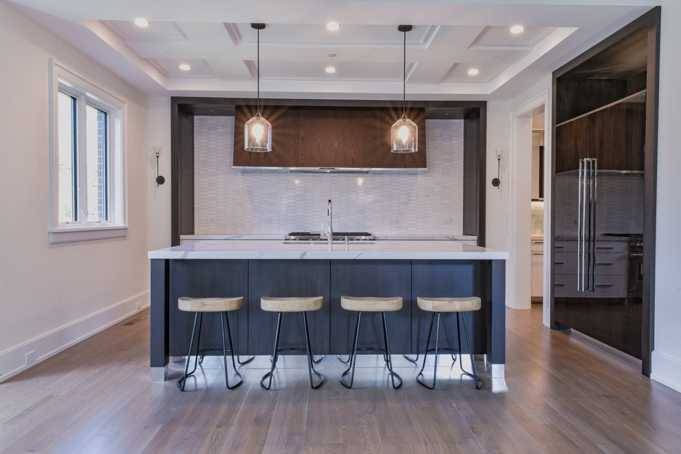 Example of a large transitional galley medium tone wood floor and gray floor open concept kitchen design in Chicago with an undermount sink, flat-panel cabinets, quartz countertops, white backsplash, marble backsplash, paneled appliances, an island, white countertops and dark wood cabinets