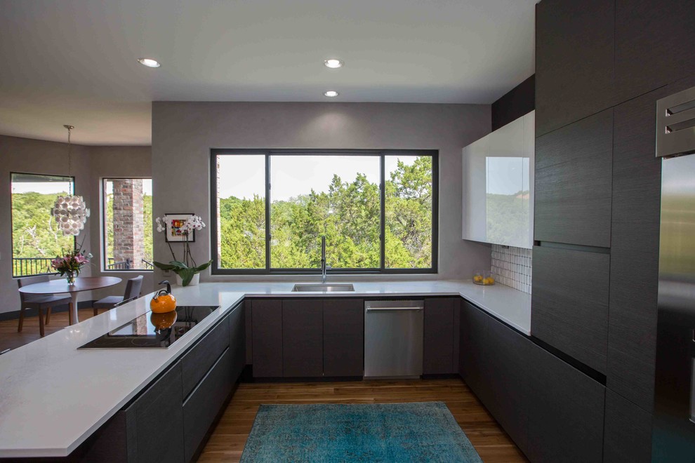 Large contemporary u-shaped eat-in kitchen in Austin with an undermount sink, flat-panel cabinets, brown cabinets, quartz benchtops, white splashback, subway tile splashback, stainless steel appliances, painted wood floors, a peninsula, brown floor and white benchtop.