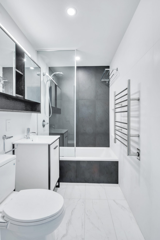 This is an example of a large modern master bathroom in New York with flat-panel cabinets, white cabinets, a drop-in tub, an open shower, a one-piece toilet, black tile, porcelain tile, white walls, marble floors, a drop-in sink, granite benchtops, white floor, an open shower, white benchtops, a niche, a single vanity and a freestanding vanity.