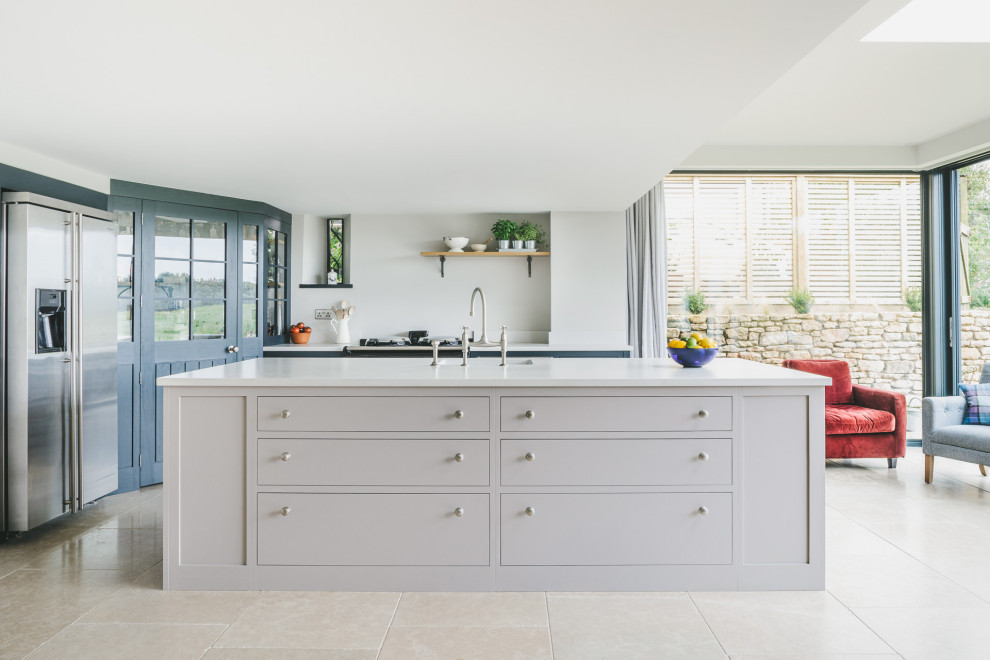 Large country l-shaped eat-in kitchen in Gloucestershire with a drop-in sink, shaker cabinets, blue cabinets, quartz benchtops, stainless steel appliances, limestone floors, with island and grey benchtop.