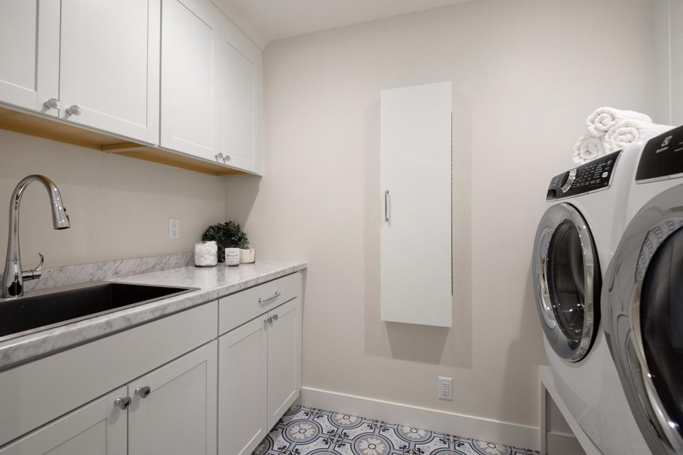 Design ideas for a mid-sized modern galley dedicated laundry room in San Francisco with a single-bowl sink, shaker cabinets, white cabinets, quartz benchtops, grey splashback, engineered quartz splashback, grey walls, a side-by-side washer and dryer, multi-coloured floor, grey benchtop and porcelain floors.