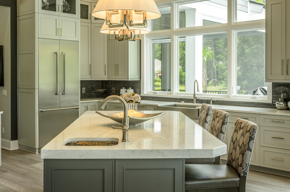 This is an example of a mid-sized transitional u-shaped eat-in kitchen in Charleston with shaker cabinets, grey cabinets, with island, a farmhouse sink, glass tile splashback, stainless steel appliances, porcelain floors, brown floor, grey splashback and quartz benchtops.