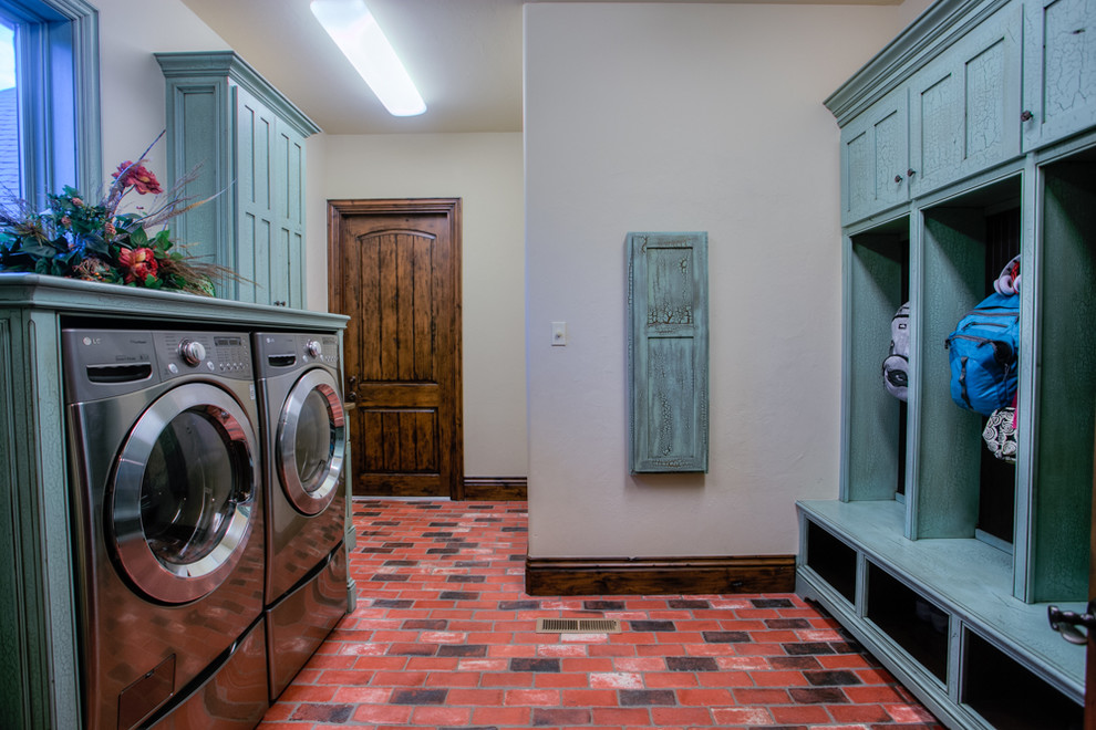 This is an example of a large country galley utility room in Oklahoma City with brick floors, blue cabinets, shaker cabinets, wood benchtops, beige walls, a side-by-side washer and dryer, red floor and blue benchtop.