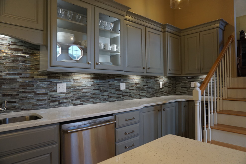 Eat-in kitchen - small traditional l-shaped medium tone wood floor eat-in kitchen idea in Providence with a triple-bowl sink, raised-panel cabinets, gray cabinets, quartz countertops, gray backsplash, mosaic tile backsplash, stainless steel appliances, an island and white countertops