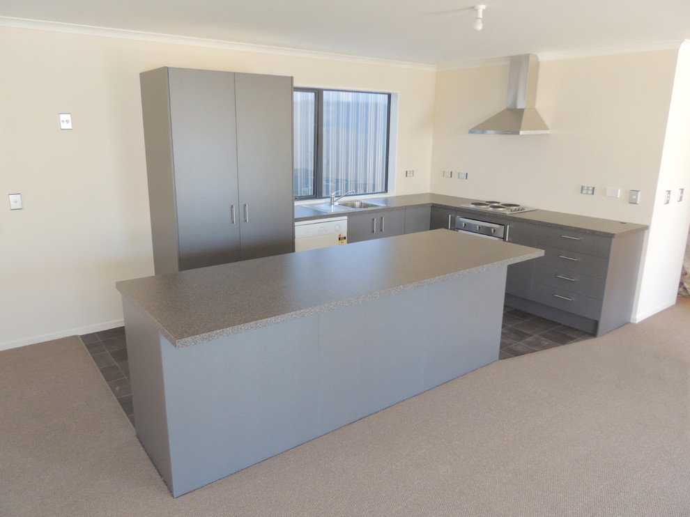 This is an example of a mid-sized modern l-shaped open plan kitchen in Christchurch with a drop-in sink, flat-panel cabinets, grey cabinets, laminate benchtops, glass sheet splashback, stainless steel appliances, vinyl floors and with island.