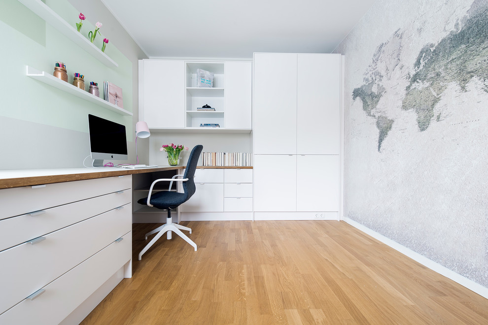 Mid-sized scandinavian study room in Berlin with beige walls, medium hardwood floors, no fireplace, a built-in desk and brown floor.