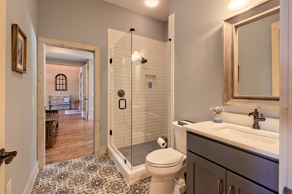 Photo of a mid-sized arts and crafts 3/4 bathroom in Atlanta with shaker cabinets, grey cabinets, an alcove shower, a two-piece toilet, white tile, subway tile, grey walls, ceramic floors, an undermount sink, engineered quartz benchtops, multi-coloured floor, a hinged shower door and white benchtops.