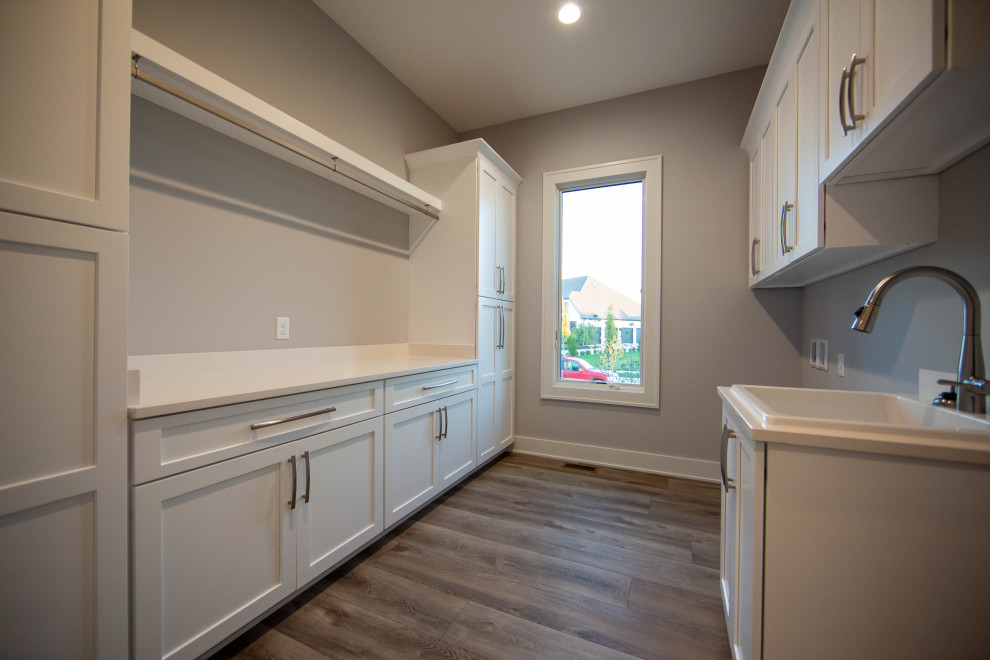 Dedicated laundry room - large modern galley laminate floor and brown floor dedicated laundry room idea in Indianapolis with a drop-in sink, shaker cabinets, white cabinets, quartz countertops, gray walls, a side-by-side washer/dryer and white countertops