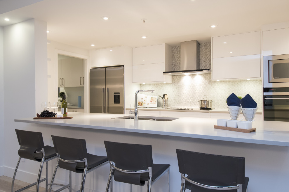 This is an example of a mid-sized contemporary galley eat-in kitchen in Vancouver with an undermount sink, flat-panel cabinets, white cabinets, quartz benchtops, white splashback, mosaic tile splashback, stainless steel appliances, light hardwood floors, with island, beige floor and white benchtop.