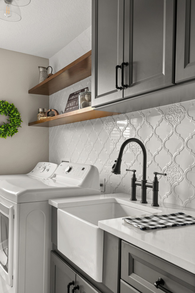Design ideas for a transitional laundry room in Orlando with a farmhouse sink, recessed-panel cabinets, grey cabinets, glass benchtops, white splashback, ceramic splashback, beige walls, a side-by-side washer and dryer and white benchtop.
