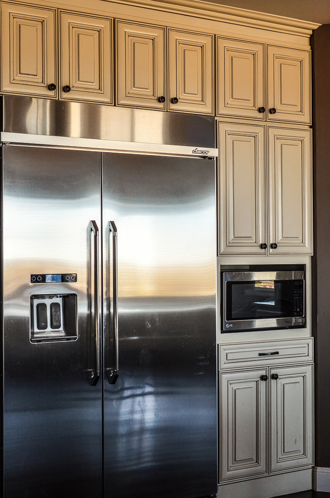 Example of a mid-sized transitional l-shaped dark wood floor and brown floor open concept kitchen design in Denver with a farmhouse sink, raised-panel cabinets, white cabinets, granite countertops, gray backsplash, porcelain backsplash, stainless steel appliances and an island