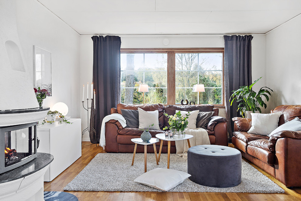 This is an example of a mid-sized scandinavian formal enclosed living room in Gothenburg with white walls, medium hardwood floors, a wood stove, a plaster fireplace surround and brown floor.