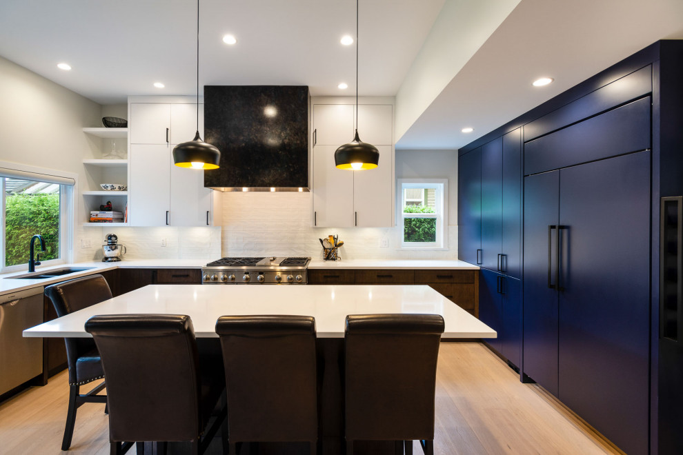 Inspiration for a mid-sized contemporary l-shaped open plan kitchen in Vancouver with a double-bowl sink, flat-panel cabinets, quartzite benchtops, white splashback, porcelain splashback, stainless steel appliances, medium hardwood floors, with island, brown floor and white benchtop.