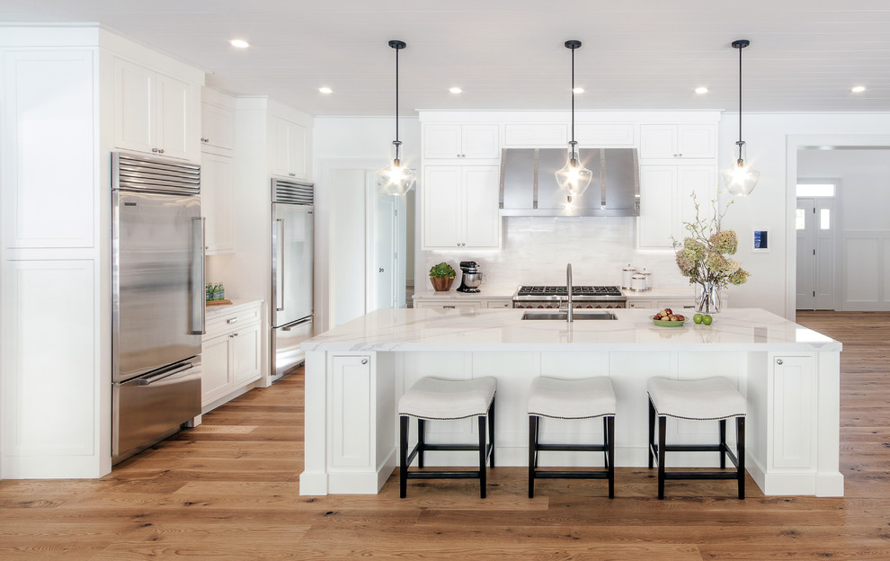 Photo of a large transitional u-shaped open plan kitchen in New York with an undermount sink, white cabinets, quartzite benchtops, white splashback, porcelain splashback, stainless steel appliances, light hardwood floors, with island, shaker cabinets and brown floor.