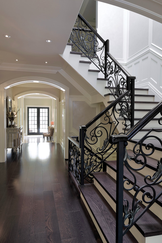 Large traditional wood u-shaped staircase in Toronto with painted wood risers and metal railing.