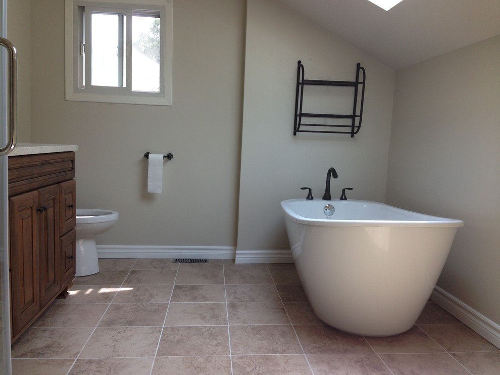 Mid-sized country master bathroom in Other with a drop-in sink, furniture-like cabinets, medium wood cabinets, quartzite benchtops, a freestanding tub, a corner shower, a one-piece toilet, black tile, cement tile, beige walls and ceramic floors.