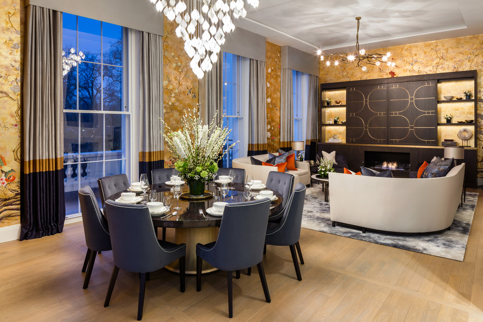 Photo of a transitional open plan dining in London with metallic walls, light hardwood floors, a standard fireplace, a wood fireplace surround and beige floor.