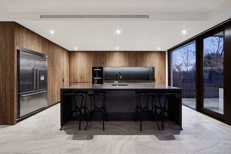 Photo of a mid-sized modern galley eat-in kitchen in Melbourne with an integrated sink, dark wood cabinets, solid surface benchtops, grey splashback, glass sheet splashback, black appliances, porcelain floors and with island.