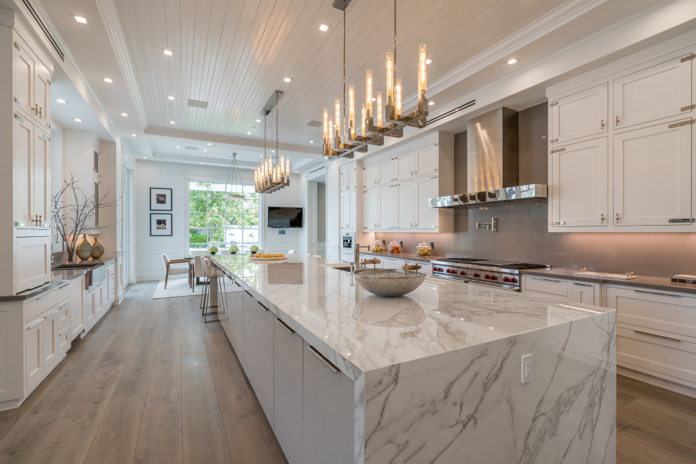 Example of a transitional galley dark wood floor and brown floor kitchen design in Los Angeles with an undermount sink, shaker cabinets, white cabinets, gray backsplash, stainless steel appliances, an island and gray countertops