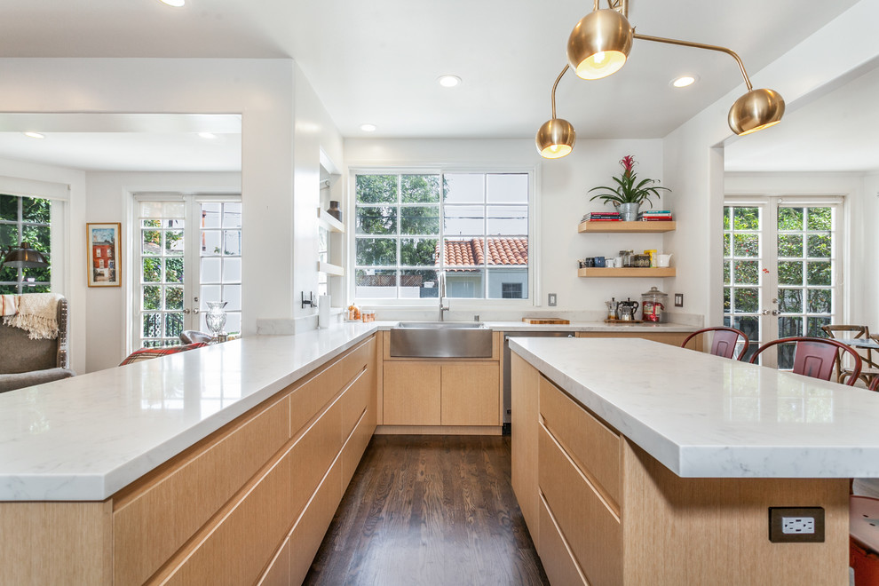 Design ideas for a mid-sized modern l-shaped open plan kitchen in Los Angeles with a farmhouse sink, flat-panel cabinets, light wood cabinets, quartz benchtops, grey splashback, cement tile splashback, stainless steel appliances, medium hardwood floors, with island, brown floor and white benchtop.