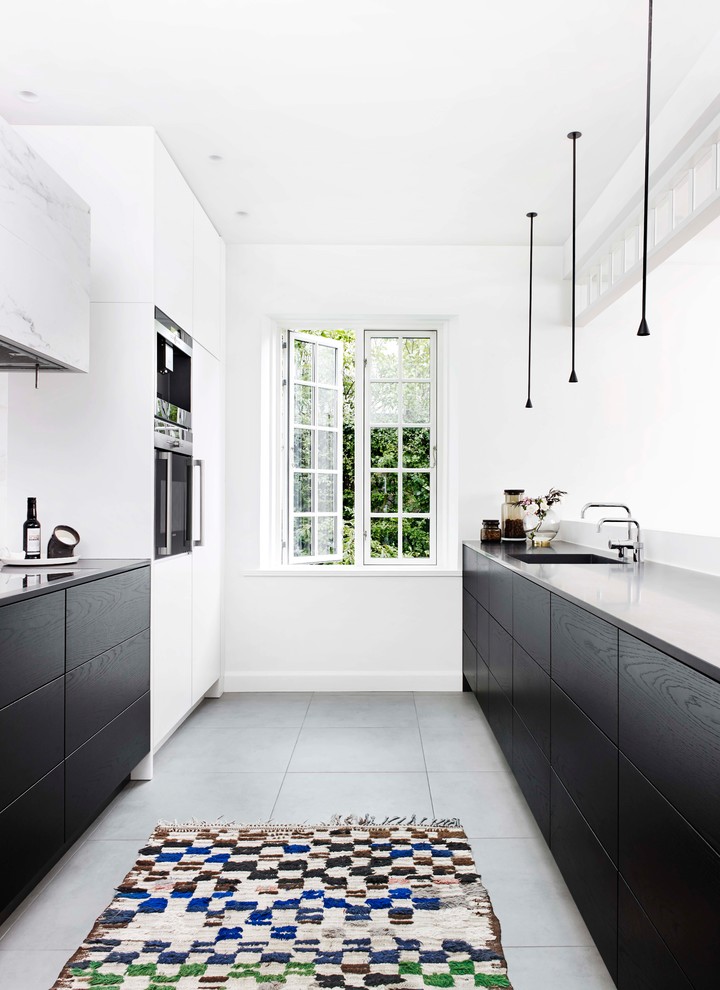 Design ideas for a mid-sized scandinavian galley separate kitchen in Copenhagen with flat-panel cabinets, black cabinets, an undermount sink, white splashback, no island, grey floor and grey benchtop.