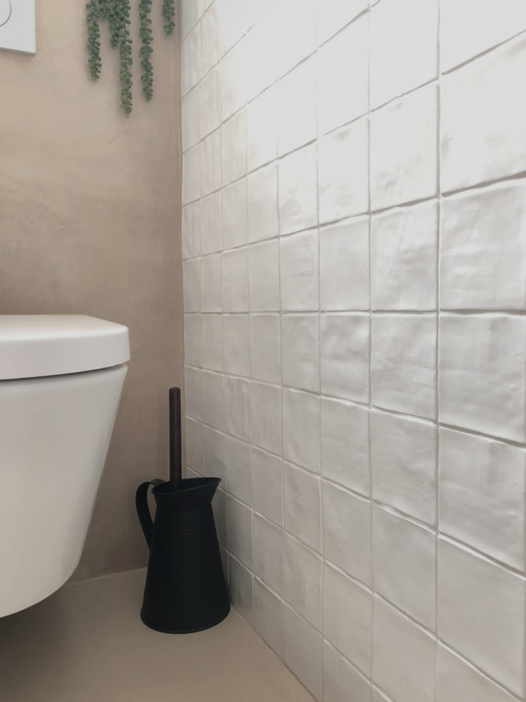 This is an example of a small traditional powder room in Paris with a wall-mount toilet, white tile, ceramic tile, a wall-mount sink, beige floor, white walls, concrete floors and white benchtops.