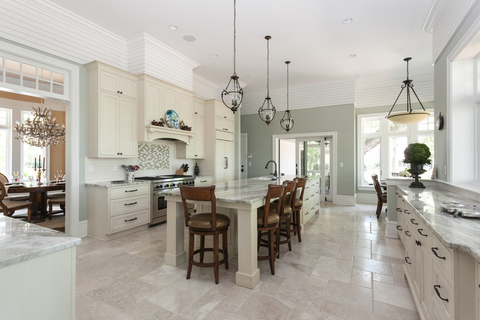 Photo of a traditional u-shaped separate kitchen in Charleston with an undermount sink, recessed-panel cabinets, white cabinets, marble benchtops, white splashback, ceramic splashback, stainless steel appliances, travertine floors and with island.