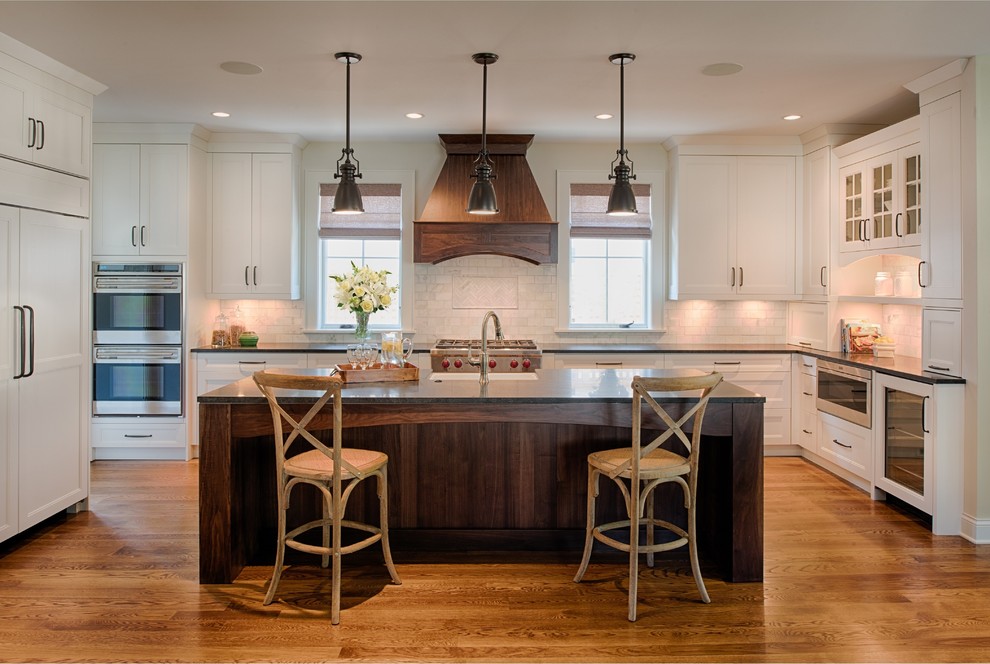 Mid-sized transitional l-shaped medium tone wood floor eat-in kitchen photo in Minneapolis with a farmhouse sink, flat-panel cabinets, white cabinets, granite countertops, gray backsplash, subway tile backsplash, stainless steel appliances and an island