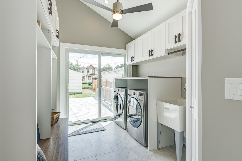 This is an example of a small transitional single-wall utility room in Indianapolis with an utility sink, shaker cabinets, white cabinets, wood benchtops, grey walls, marble floors, a side-by-side washer and dryer, grey floor and brown benchtop.