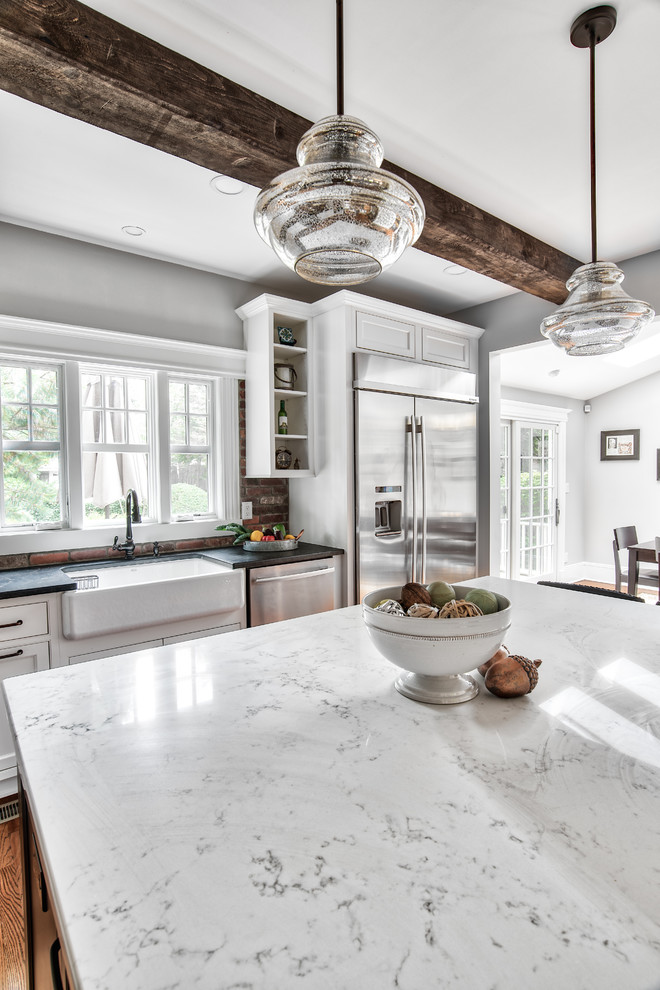 This is an example of a large country l-shaped eat-in kitchen in New York with a farmhouse sink, beaded inset cabinets, white cabinets, granite benchtops, brick splashback, stainless steel appliances, with island, brown floor, black benchtop and painted wood floors.