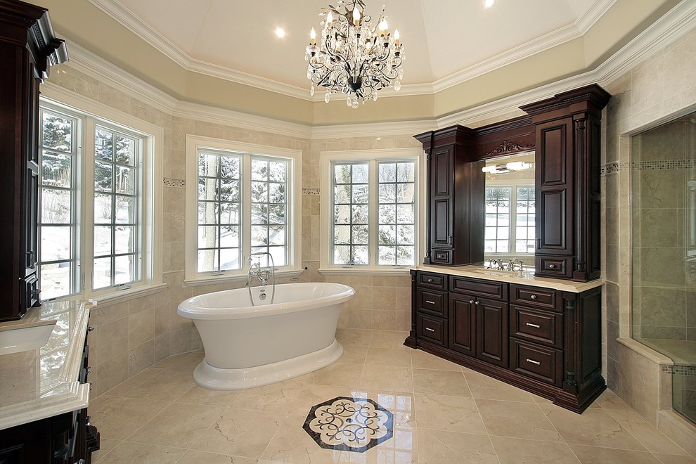 Design ideas for a traditional bathroom in Omaha with an undermount sink, raised-panel cabinets, dark wood cabinets, a freestanding tub, an alcove shower, beige tile, beige walls, limestone floors, beige floor and a hinged shower door.