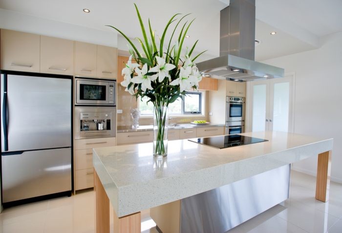 Mid-sized contemporary galley open plan kitchen in Sunshine Coast with a drop-in sink, flat-panel cabinets, light wood cabinets, quartz benchtops, beige splashback, glass sheet splashback, stainless steel appliances, porcelain floors and with island.